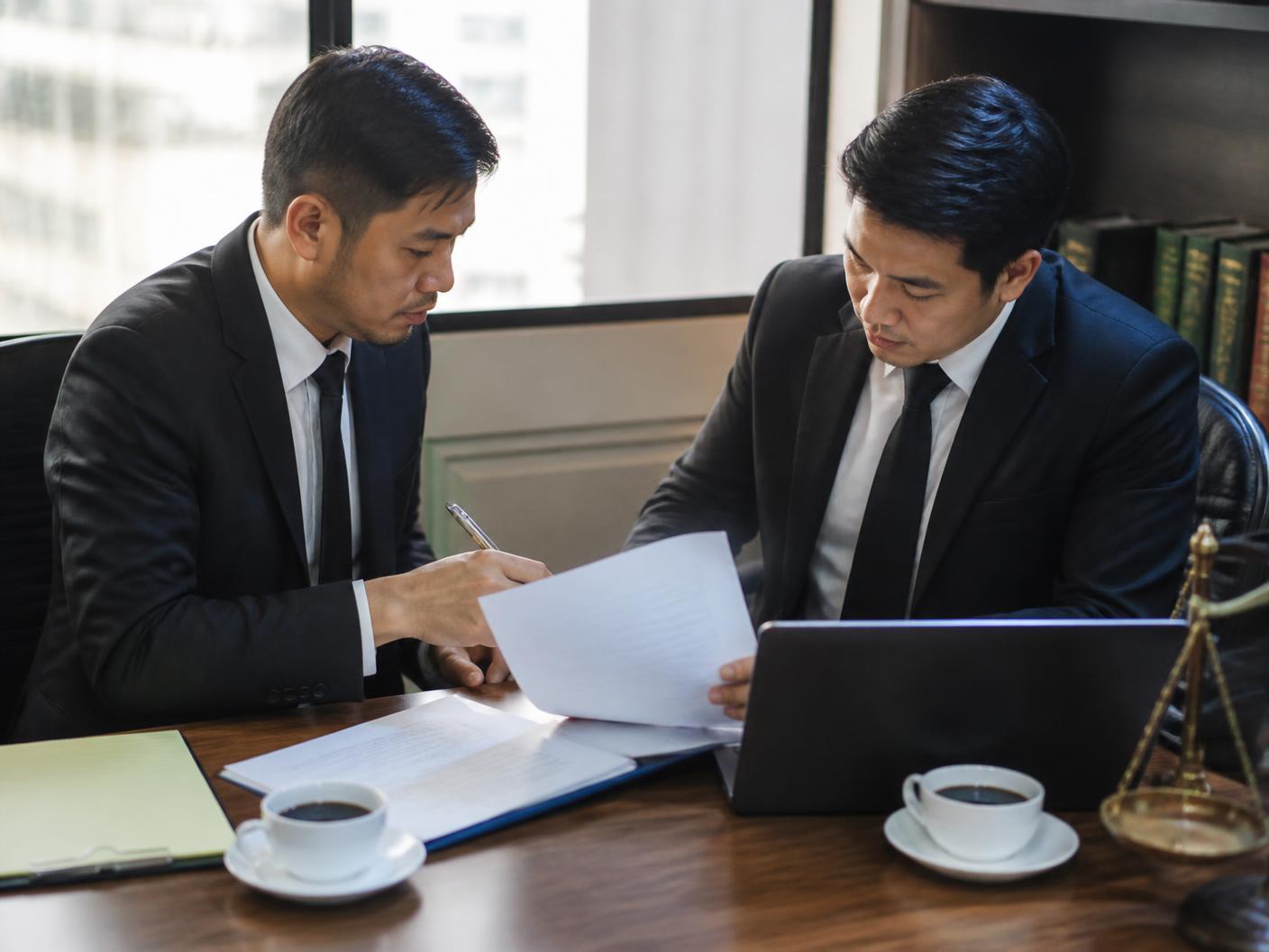 ทนายความสองคนตรวจถ้อยคำในร่างคำฟ้องร่วมกันบนโต๊ะประชุมสำนักงานกรุงเทพ
